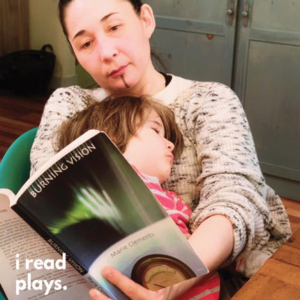 Reneltta Arluk reads Burning Vision while holding her child.