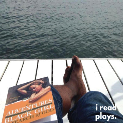 A copy of The Adventures of a Black Girl in Search of God sits on Quincy Armorer's lap on a pier looking out onto a lake