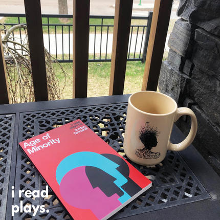 A copy of Age of Minority sits on a table on a patio next to a mug